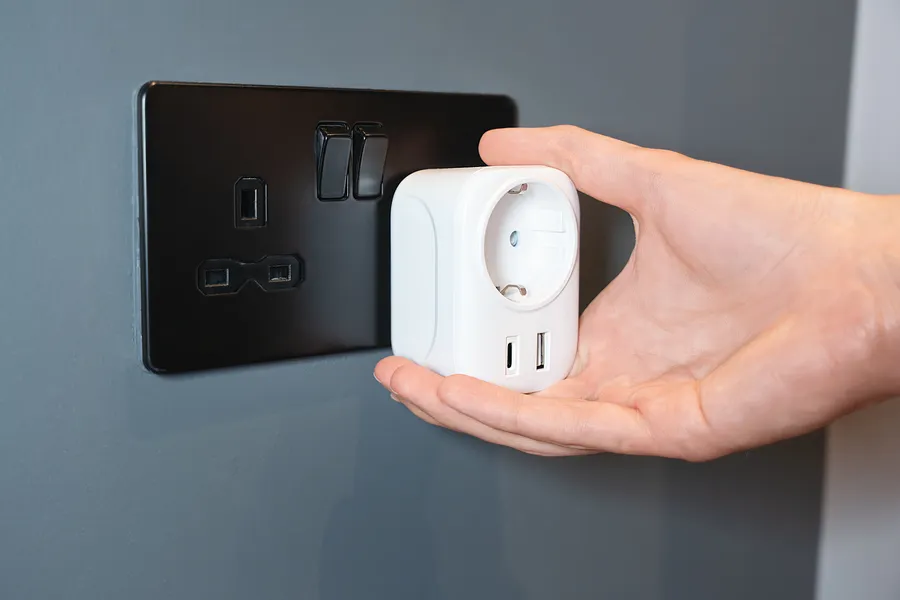 Käsi, joka asettaa älypistorasian seinäpistorasiaan, jossa on USB-portteja.