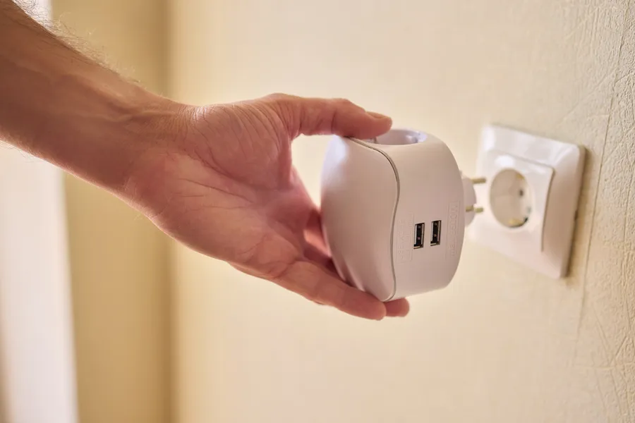 Mies kytkee älypistorasian seinään, jossa on USB-portteja. Taustalla vaalean värinen seinä.
